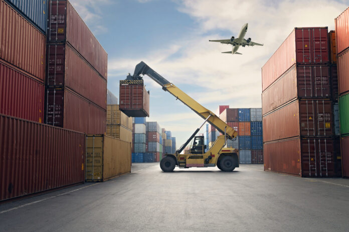 Airplane flying above container port.